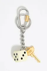 Llavero con mosquetón de metal plateado y cierre dorado, cadena de eslabones plateados, dije de dado blanco con puntos negros y dije de llave dorada con inscripción.