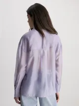 Camisa Calvin Klein de lyocell color lila, de corte holgado, manga larga, cuello en punta, cierre de botones, bolsillos con solapa en el pecho y logo bordado en el bolsillo del pecho.