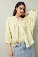Camisa color amarillo pálido a rayas finas, con cuello mao, mangas 3/4 abullonadas y cierre frontal con botones.