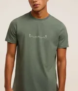 Remera verde militar de algodón, corte regular, cuello redondo, manga corta y estampa frontal con diseño de montañas y excursionistas en línea continua blanca.