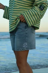 Short de jean celeste con logo estampado en blanco en la pierna izquierda.