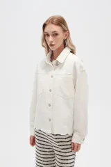 Campera de jean color crudo, de corte recto, con cuello clásico, cierre frontal con botones metálicos, dos bolsillos con solapa en el pecho y bajo con detalle de bordado calado.