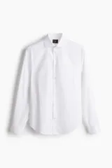 Camisa blanca de algodón con cuello italiano, tapeta clásica y canesú en la espalda. Mangas largas con tapeta y botón, y cierre ajustable de botón en los puños. Bajo levemente redondeado y corte ajustado.