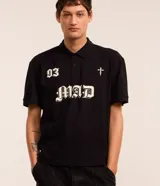 Remera boxy de mangas cortas, confeccionada en algodón, color negro, con cuello polo y lettering "93 MAD" y una cruz estampada en la parte delantera.