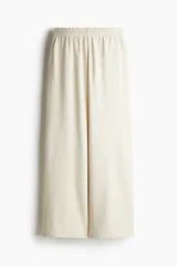 Pantalón de felpa color crema, de corte relajado con cintura elástica fruncida, bolsillos laterales discretos y piernas rectas.