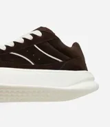 Championes de estilo skater para hombre, confeccionados en poliuretano color tostado. Poseen punta redonda, caña baja, suela alta blanca y cierre mediante cordones anchos tipo fat lace. Incluyen recortes y detalles contrastantes en los laterales.