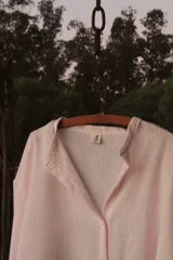 Camisa oversize color rosa claro a rayas verticales blancas, con cuello mao y mangas largas con puños elásticos.