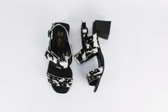 Sandalias de cuero con estampado animal print de vaca en blanco y negro, con detalles de tachas plateadas. Tienen correa trasera con hebilla y taco cuadrado de 5 cm.