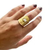 Anillo dorado con textura y piedra blanca ovalada engarzada.
