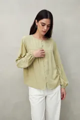 Camisa celeste de corte holgado con botones frontales, canesú con tablas y mangas 3/4 amplias con puño elastizado.