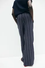 Pantalón de corte holgado en tejido liviano de mezcla de lino a rayas verticales blancas y azul marino. Modelo de tiro alto con cintura elástica y cordón para ajustar fino, bolsillos laterales discretos y piernas rectas.