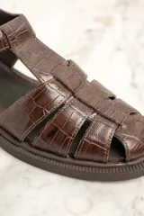 Sandalias cangrejeras de cuero marrón con textura croco, hebilla dorada y suela plana.