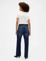 Jean de corte recto y relajado, con tiro medio y lavado oscuro. Presenta diseño clásico de cinco bolsillos, cierre frontal con cremallera y botón metálico.