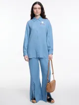 Camisa celeste de calce relajado con abertura en la espalda y mangas largas. Confeccionada en tejido liviano de lino y viscosa. Incluye tres pins decorativos.