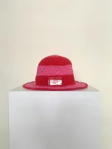 Sombrero tipo bucket tejido a crochet a mano, con hilo 100% algodón y diseño a rayas en tonos rosa y rojo. Presenta una etiqueta con el logo de la marca Cilento en el frente.