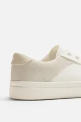 Zapatillas deportivas blancas con detalle de color a contraste en el talón y suela con acabado irregular.