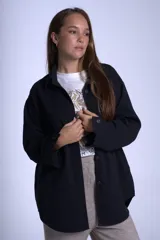 Sobrecamisa negra de gabardina con cuello camisero, cierre frontal con botones, mangas largas con puños abotonados y bolsillos de parche en el pecho.