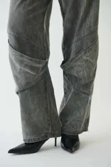 Pantalón jean gris de tiro medio con calce amplio, bolsillos delanteros y traseros, recortes en las piernas, trabillas para cinturón y cierre con botón y cremallera.