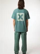 Camiseta de manga corta color azul grisáceo, con un gran estampado cuadrado turquesa en la espalda que contiene una 'X' blanca. Pequeño logo bordado en la parte superior de la espalda.