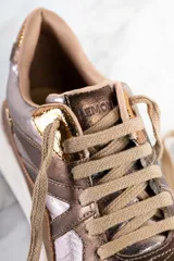 Zapatillas deportivas de cuero metalizado color cobre y plateado, con cordones color beige, suela de goma blanca y logo de la marca en el lateral.