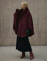 Ruana o poncho negro de tejido suave, con cuello y puños adornados con apliques de piel sintética (faux fur).