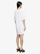 Vestido blanco de manga corta, estilo camiseta, confeccionado en jersey de algodón orgánico. Presenta un lazo frontal ajustable que genera un efecto drapeado y un recorte bordado en el frente.