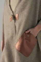 Chal beige con bolsillos de cuero y terminaciones en flecos, diseñado para un ajuste cómodo en los hombros.