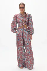 Conjunto de pantalón y blusa de lino con estampado floral en tonos terracota y azul. La blusa es de manga larga con cuello mao y se ata en la parte delantera. El pantalón es culotte de tiro alto con bolsillos laterales y cierre frontal escondido.