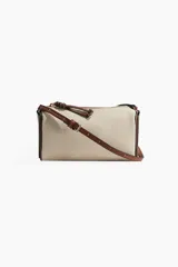 Bandolera rectangular de tela color beige con textura tipo canasta y detalles en cuero marrón. Tiene cierre superior con cremallera, correa larga regulable con hebilla y forro interior.