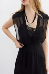 Vestido largo negro de viscosa georgette, con caída fluida y lazo trenzado en la cintura. Presenta doble capa en la parte superior que combina recortes y transparencias.