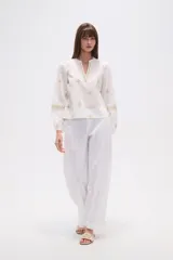 Blusa de algodón color tostado con bordados geométricos en blanco y azul marino, cuello mao con escote en V y mangas largas abullonadas con puños elásticos.