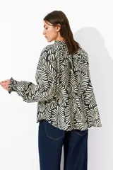 Blusa oversized con estampado de hojas en blanco y negro, cuello con volados y lazos, mangas largas raglán con puños elásticos y bajo redondeado.
