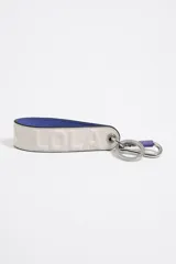 Llavero de cinta de piel color beige claro con logo en relieve y forro interior color azul eléctrico. Incluye mosquetón y anilla metálicos.