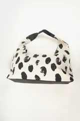 Bolso tipo tote bag con estampado de lunares irregulares en blanco y negro, con base y asas cortas en color negro.