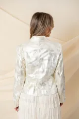 Chaqueta corta de cuero ecológico laminado color plateado, con cierre frontal asimétrico, cuello con solapas y tachas, y presillas en los hombros.
