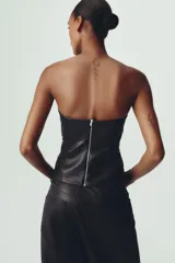 Top tipo corsé negro de cuero sintético, con escote corazón y hombros descubiertos. Detalle de costuras marcadas y cierre trasero con cremallera.
