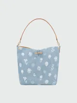 Bolso tipo cubo Longchamp modelo Le Roseau Denim, color gris oscuro con estampado de flores blancas. Tiene asa corta de cuero marrón y cierre con botón a presión. Incluye correa larga extraíble y ajustable.
