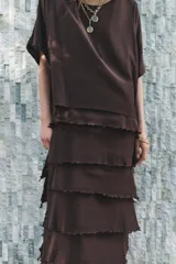 Vestido midi color marrón oscuro confeccionado en hilatura con viscosa y algodón. Tiene cuello redondo, manga corta y bajo con volantes desflecados y aberturas laterales.
