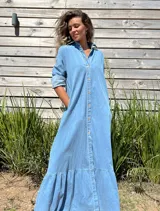 Vestido camisero largo de jean celeste con botones frontales, cuello camisero y volado en el ruedo.