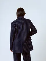 Blazer azul marino con rayas verticales blancas, de corte clásico, con solapas de muesca, cierre frontal con dos botones, bolsillos con solapa y abertura en la espalda.