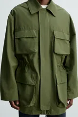 Parka verde militar de corte relaxed fit confeccionada en tejido técnico ligero. Cuello solapa y manga larga. Bolsillos de plastrón con solapa en delantero. Cintura ajustable en interior. Cierre frontal con cremallera oculta por solapa con botones a presión.