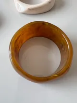 Brazalete rígido de acrílico color marrón claro con forma irregular.