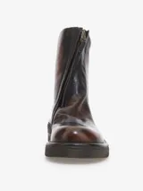 Bota corta de cuero bovino con efecto envejecido en tonos marrón oscuro y caramelo. Presenta cierre frontal con cremallera y suela de goma gruesa con relieve. El tacón bajo tiene un detalle metálico horizontal en color cobre.