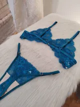 Conjunto de lencería de dos piezas (corpiño y bombacha tipo colaless/tanga) de encaje floral, color verde petróleo/turquesa oscuro. El corpiño es triangular con tirantes ajustables y la bombacha es de corte bajo con bordes festoneados.