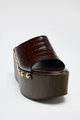 Mules de cuero marrón con plataforma de madera y detalle de tachas doradas.