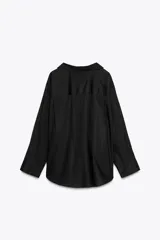 Camisa negra de cuello solapa y manga larga amplia. Tiene un bolsillo de parche en el delantero, detalle de pliegues y cierre frontal con botones.