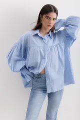 Camisa gris a rayas verticales blancas, de corte amplio, cuello alto con lazo y mangas largas abullonadas con puños elásticos.