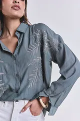 Camisa celeste con bordado de hojas blancas en el frente, de corte clásico y mangas largas.