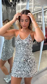 Vestido corto plateado con lentejuelas, breteles finos y escote en V.