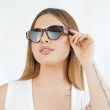 Lentes de sol negros con forma ovalada y detalles dorados en el marco.